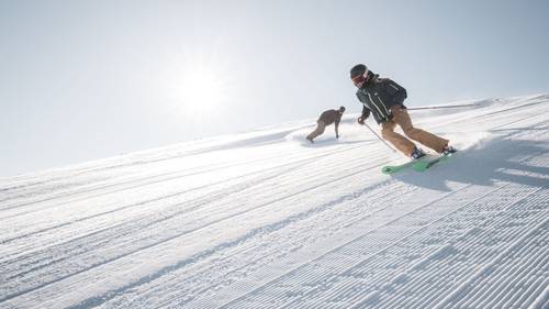 A skier and a snowboarder carving down the mountain