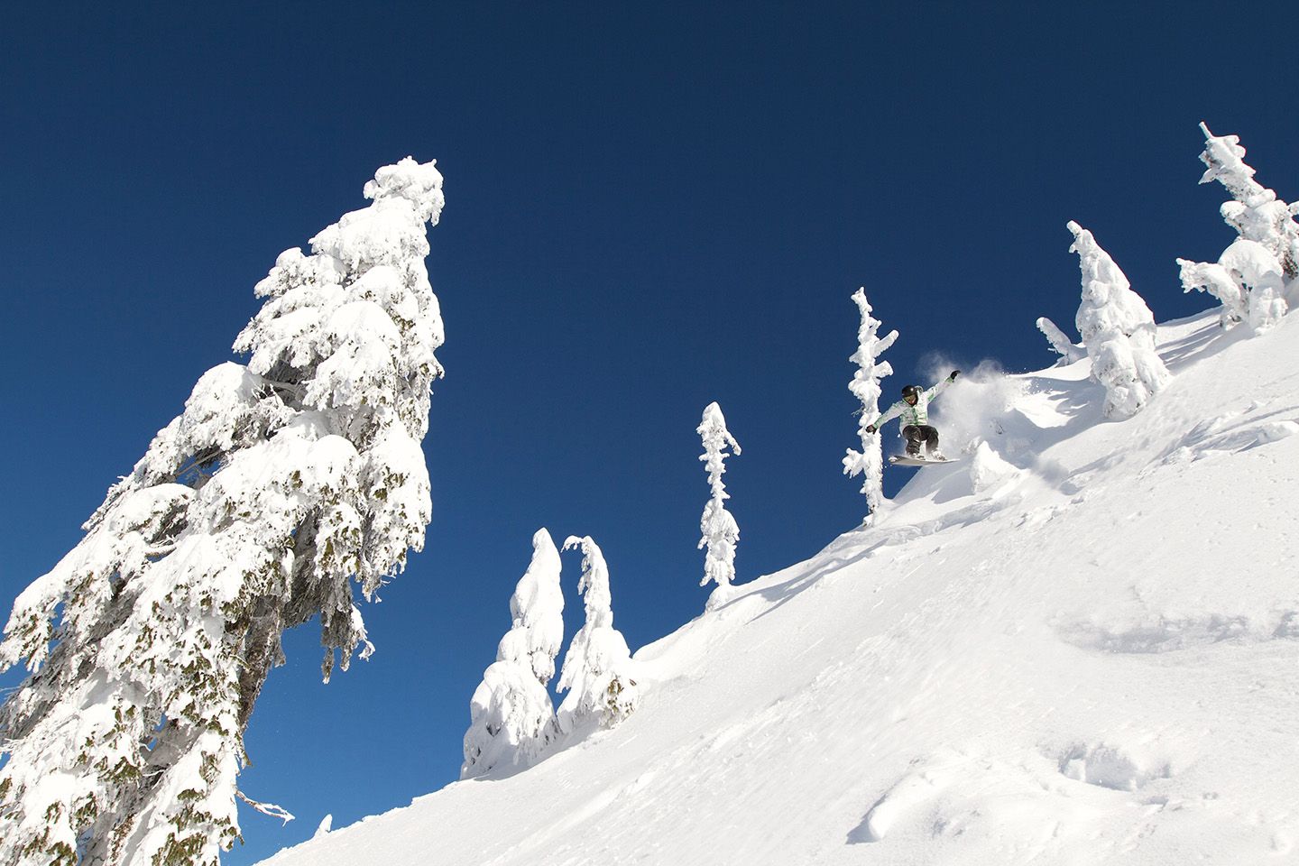 A snowboarder in the air over a natural feature on a powder day under blue sky.
