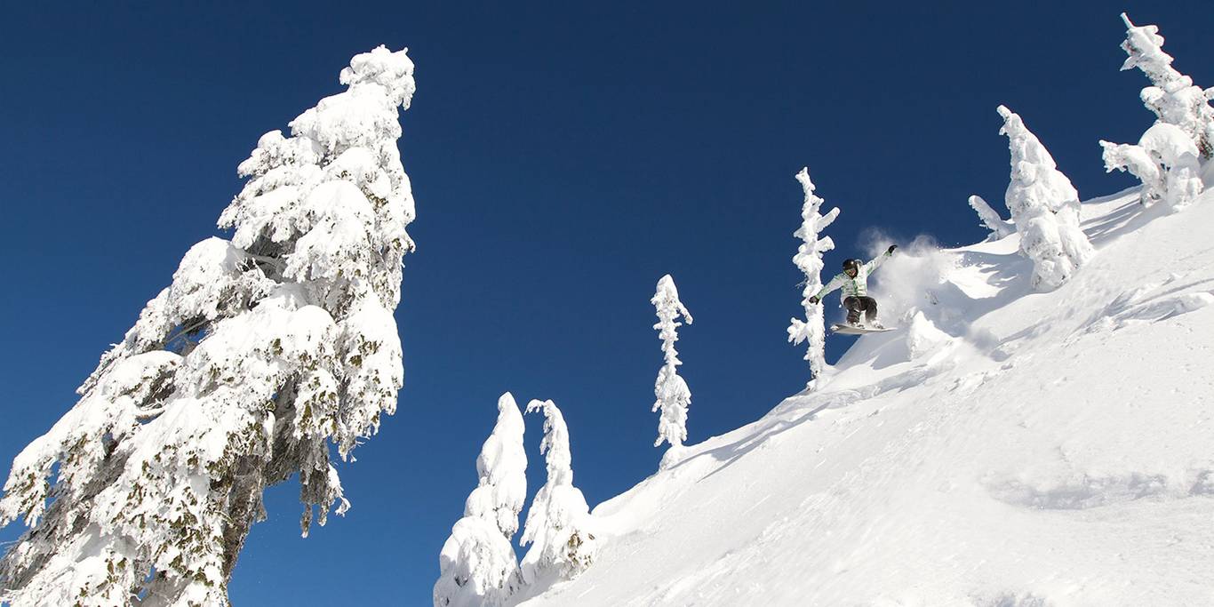 A snowboarder in the air over a natural feature on a powder day under blue sky.