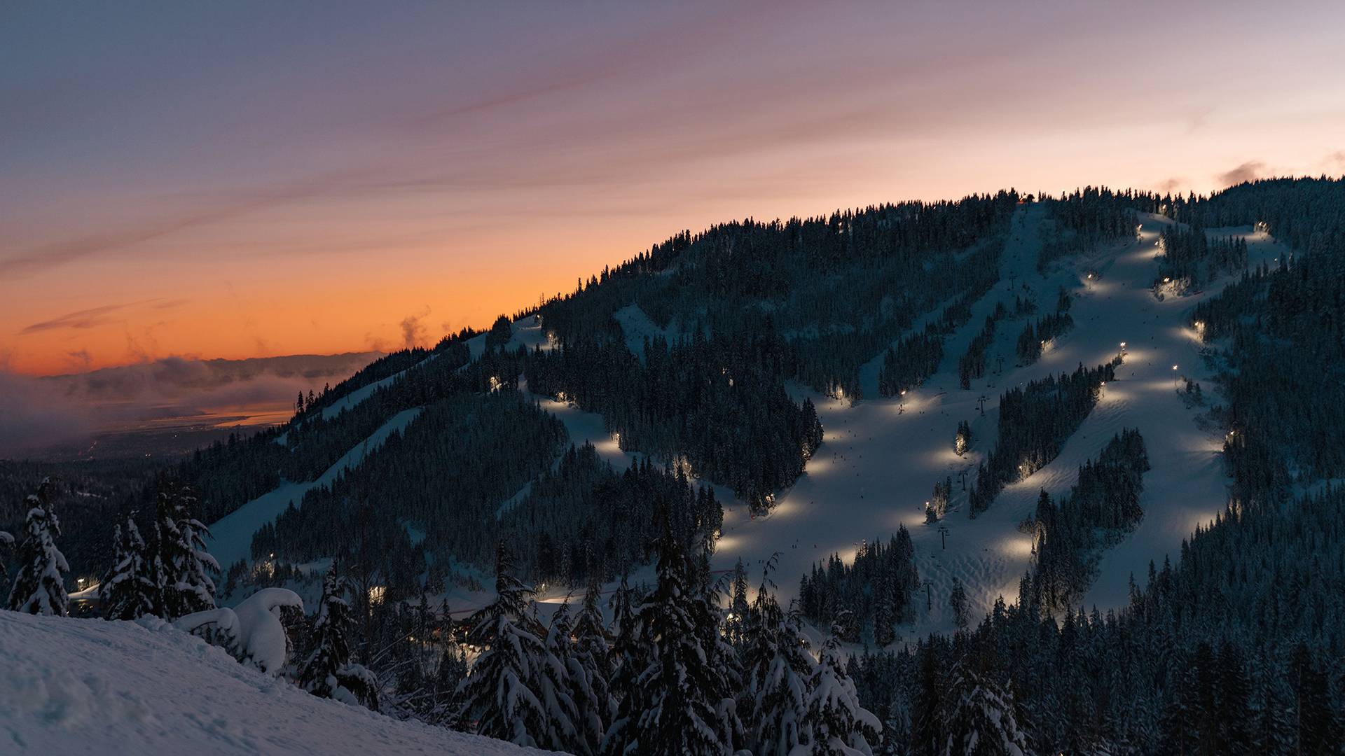 A snowy mountain at dusk with lit up ski runs.