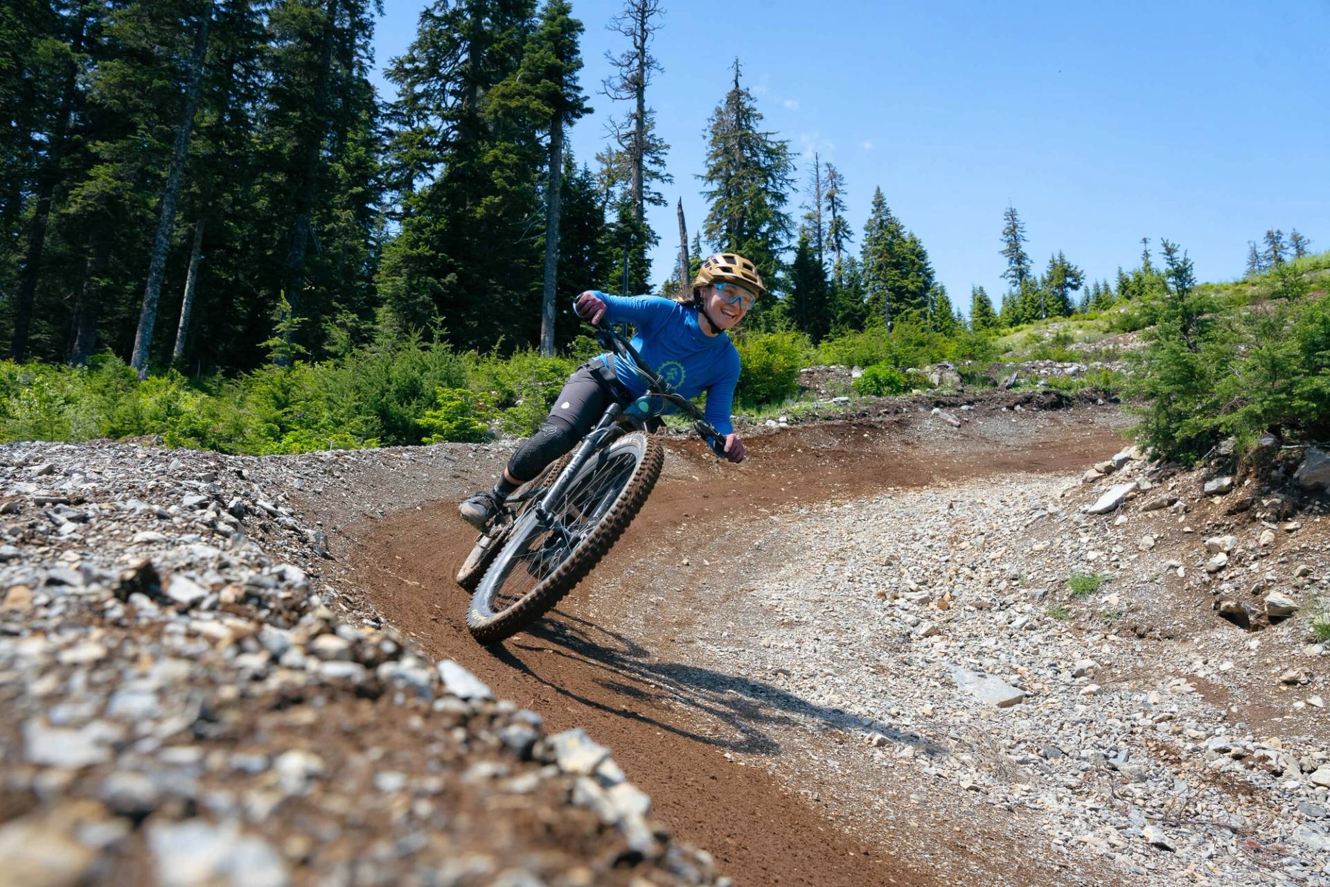 woman in evergreen mountain bike alliance jersey riding mountain bike on a berm while smiling.