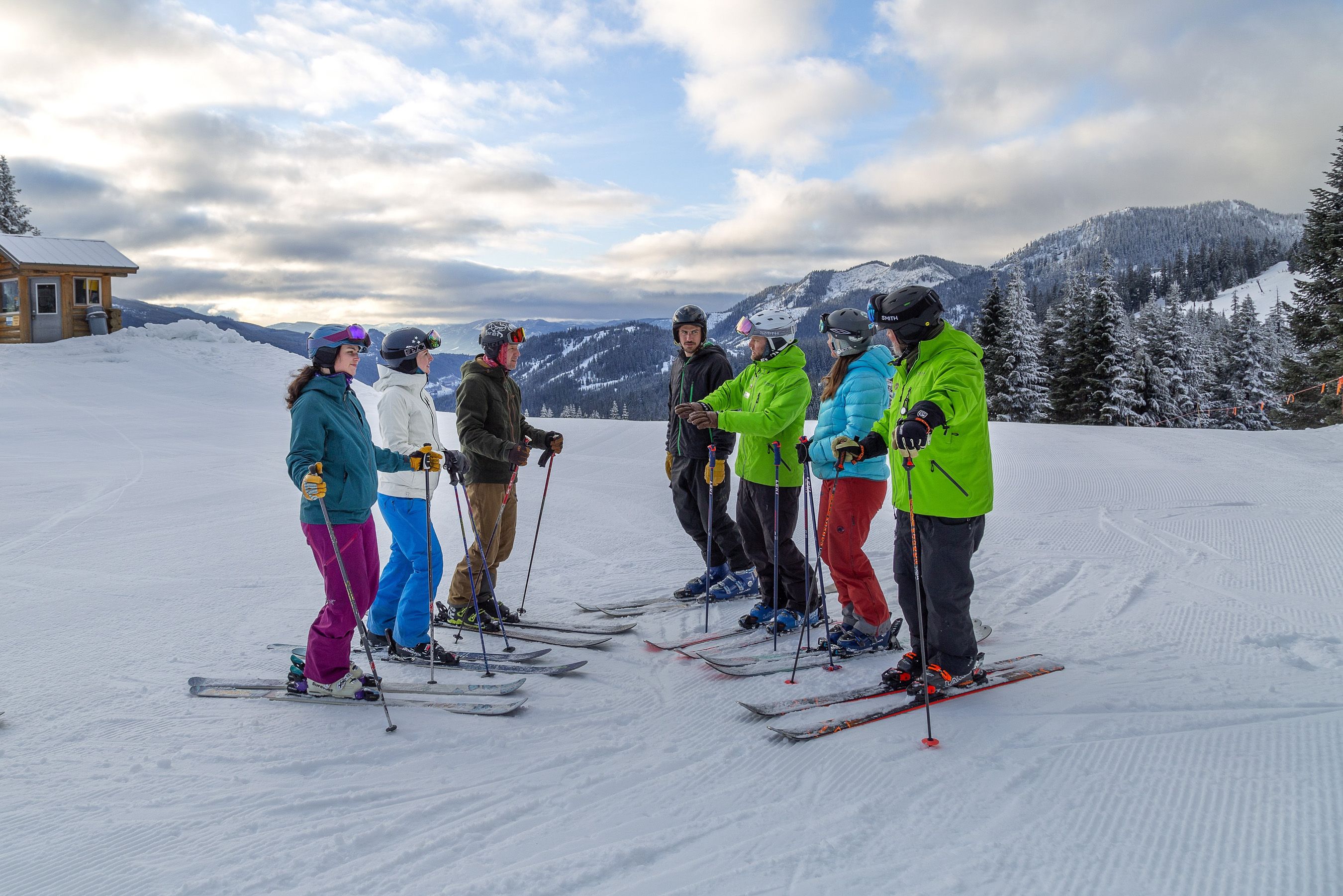 group of adults with ski instructor at top of mountain in ski lesson