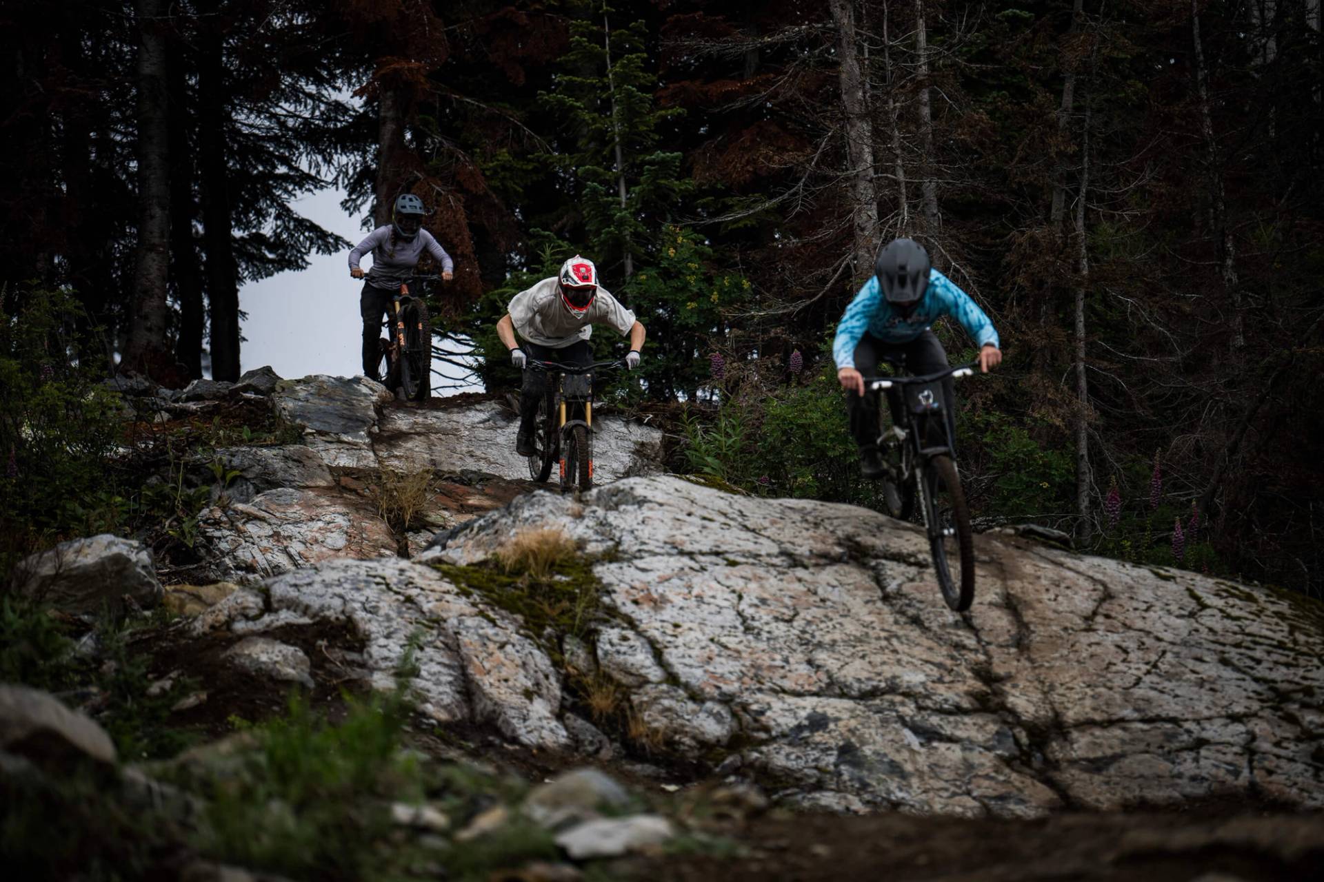 group of three mountain bikers riding down a rock slab in succession.