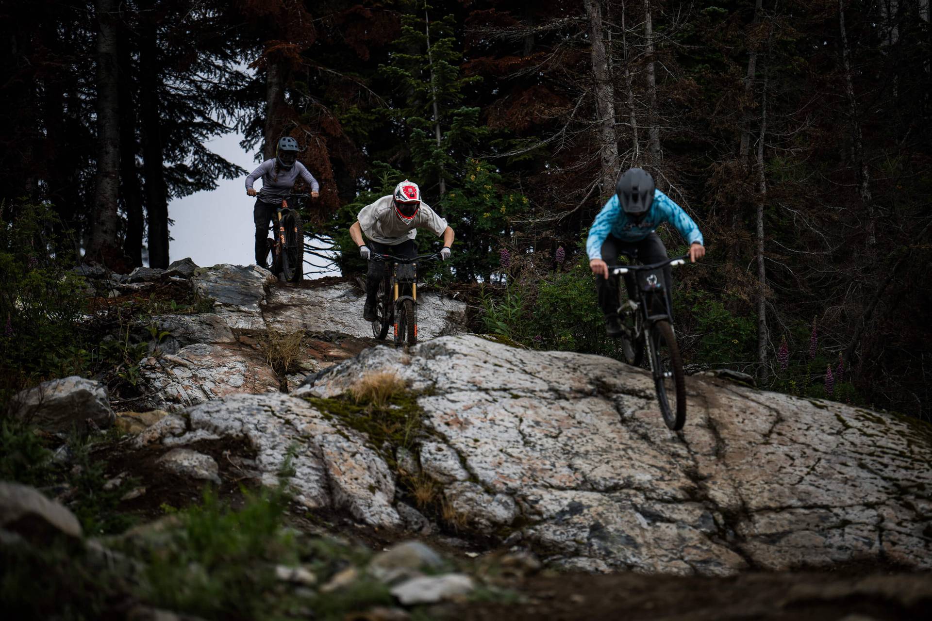group of three mountain bikers riding down a rock slab in succession.