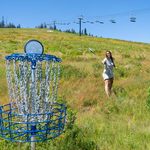 girl throwing disc at disc golf basket