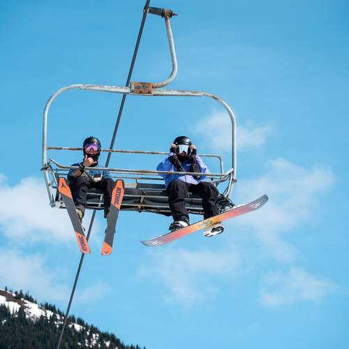 Skier and snowboarder waving from chairlift