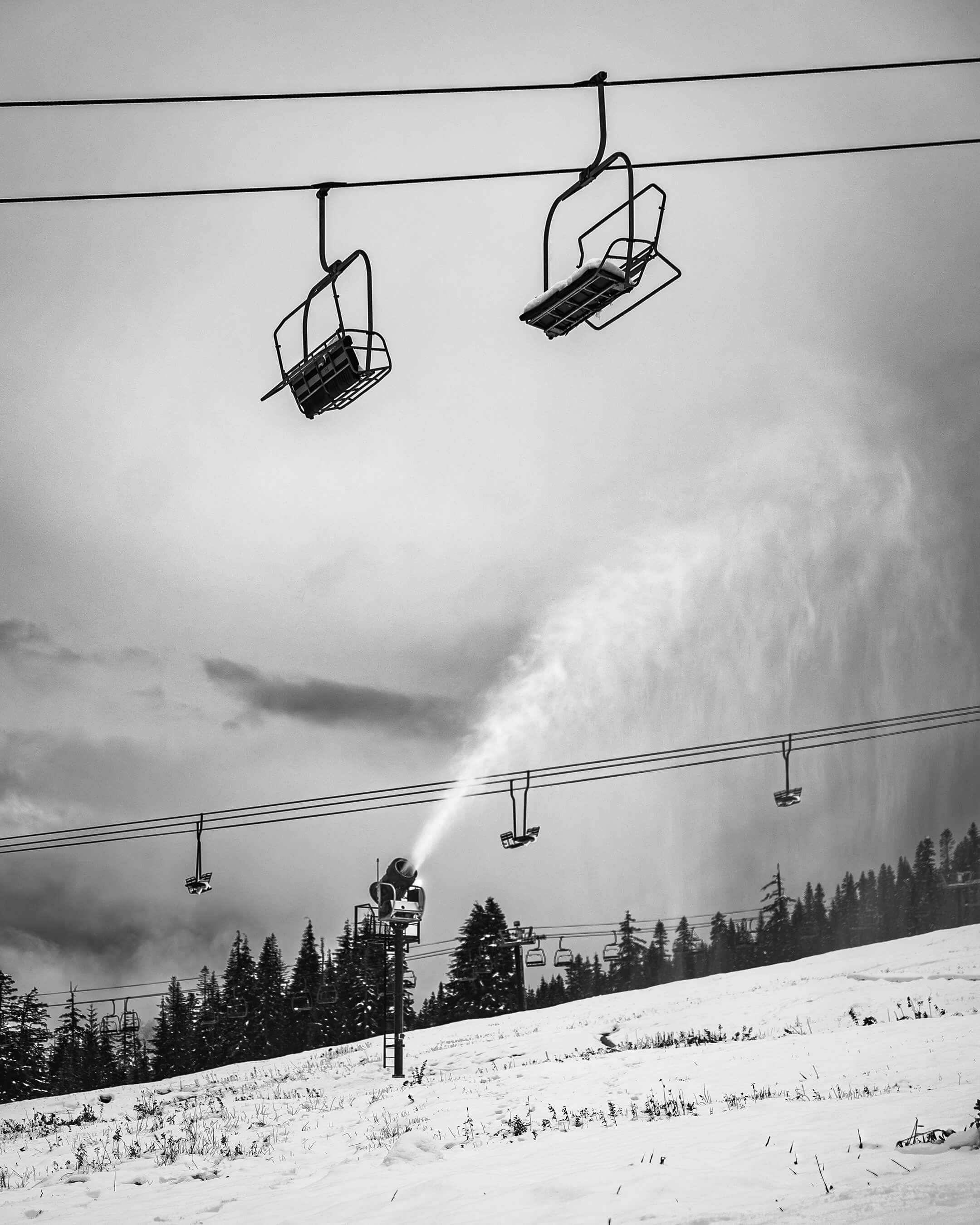 Snow gun blowing snow with chairlift in background