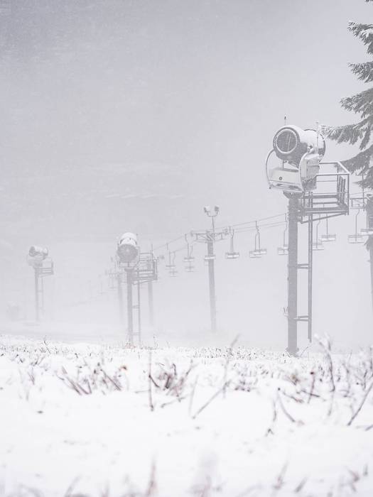 Grass poking through snow with snow guns in background