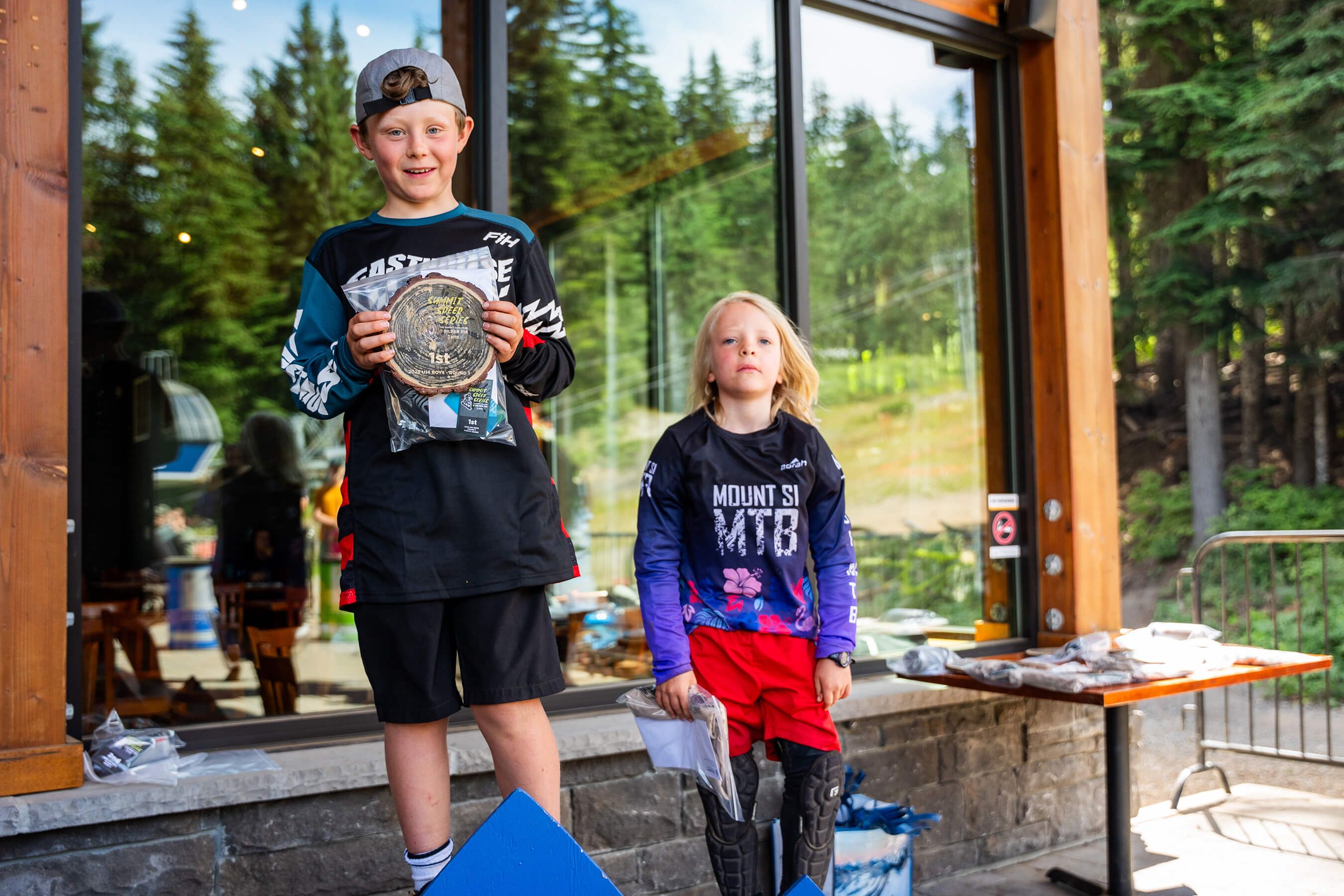 two kids standing on a podium with their prizes smiling