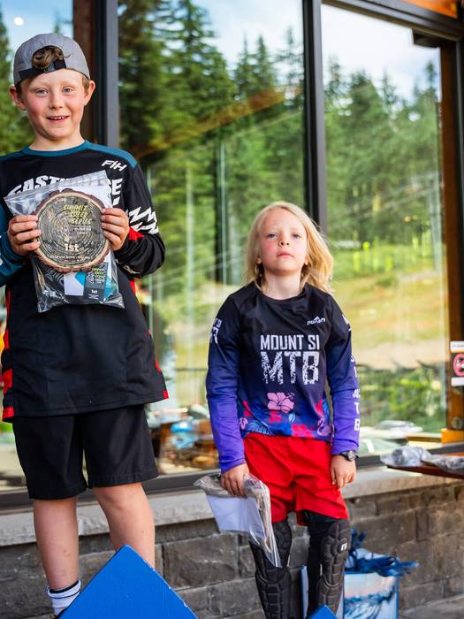 two kids standing on a podium with their prizes smiling