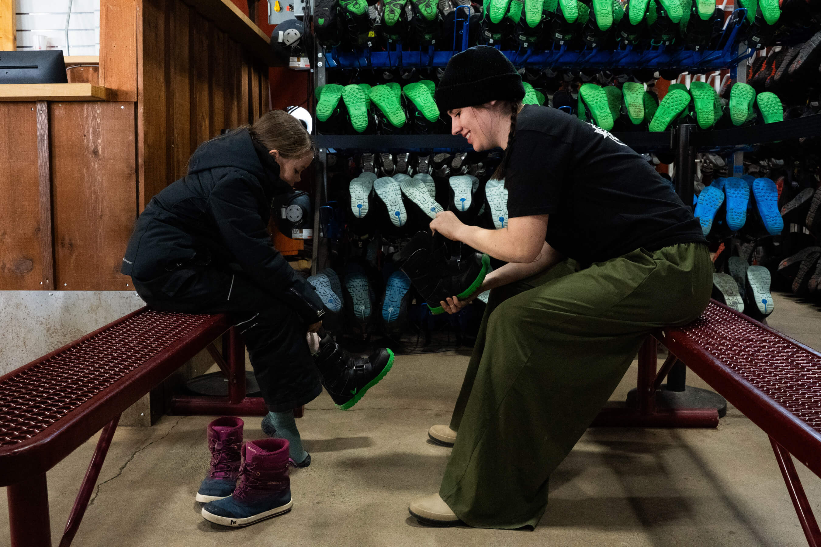 A rental tech helping a child put on snowboard boots
