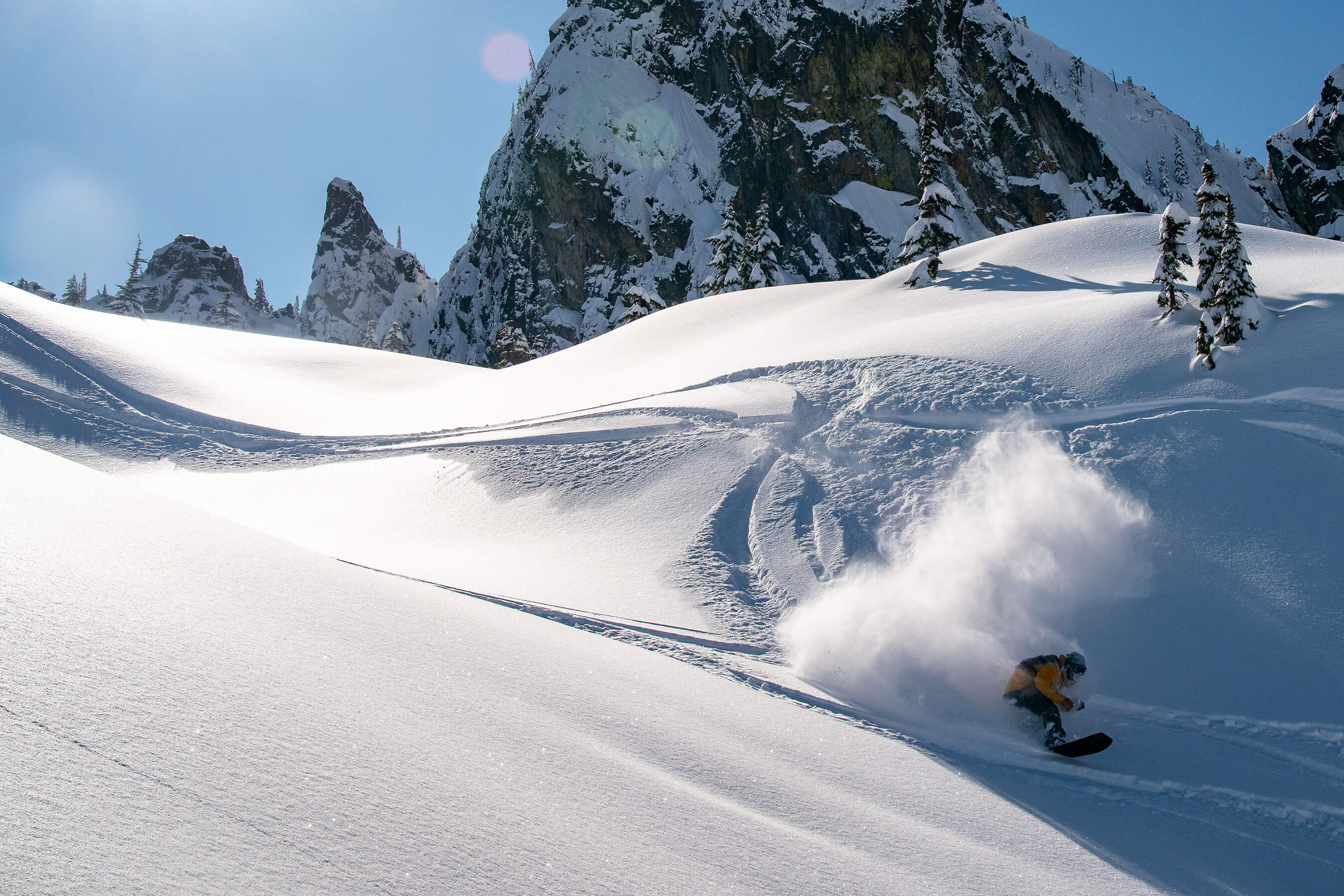 A snowboarder makes fresh tracks under bluebird skies and jagged peaks