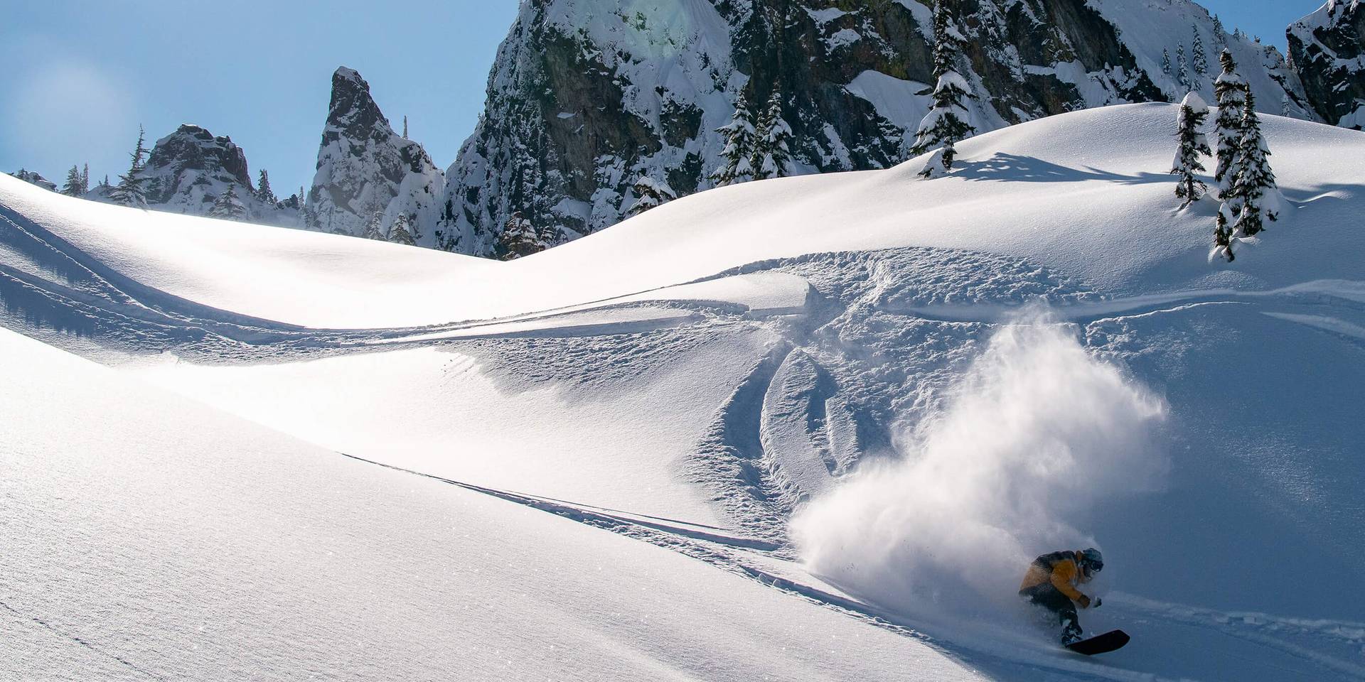 A snowboarder makes fresh tracks under bluebird skies and jagged peaks