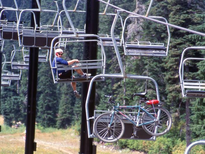 mountain biker on a chairlift with a bike hanging off the chair behind them