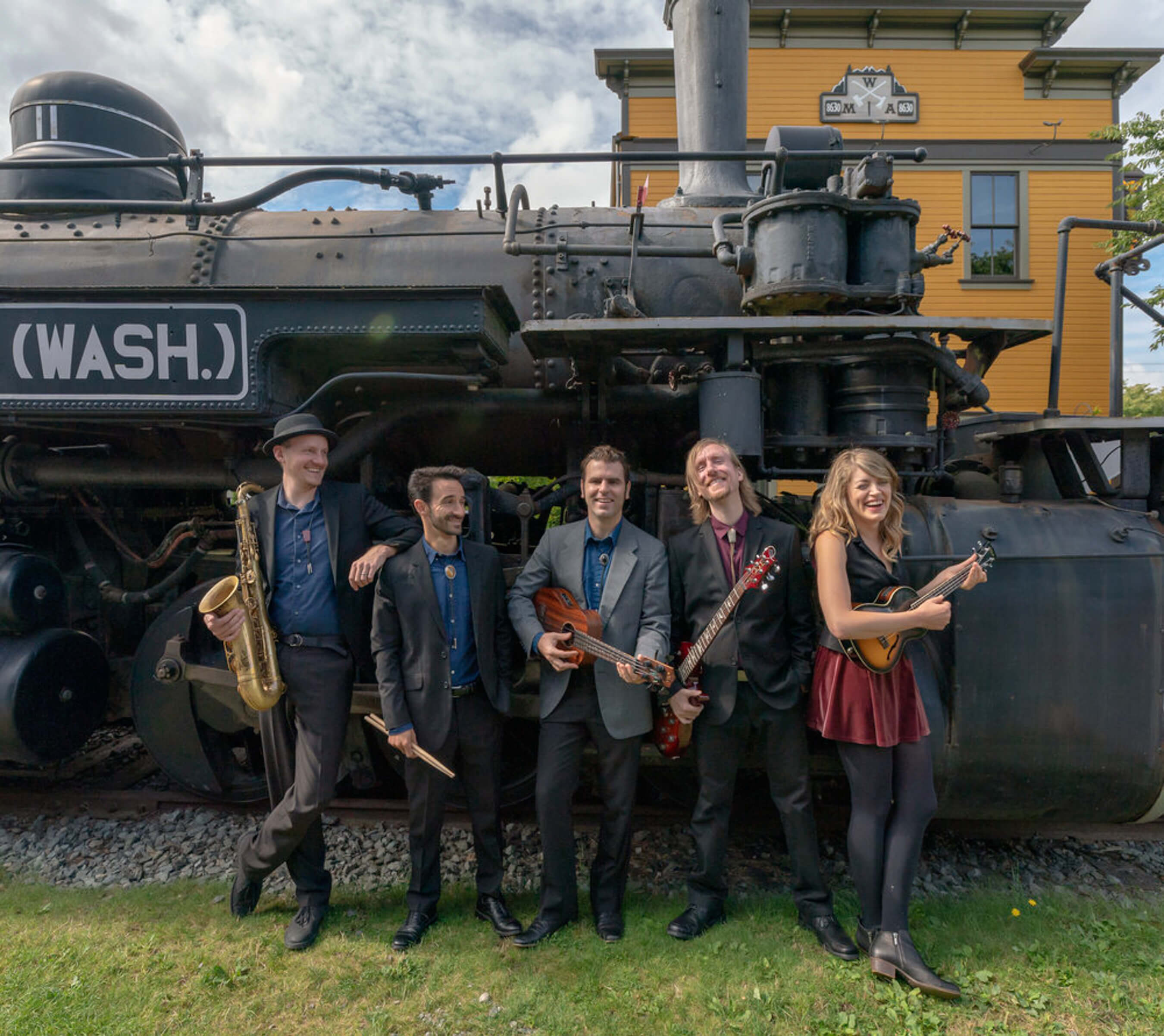Birch Pereira and the Gin Joints band poses with instruments in front of train