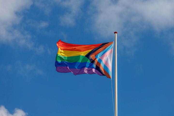 Progress Pride flag flying against a blue sky