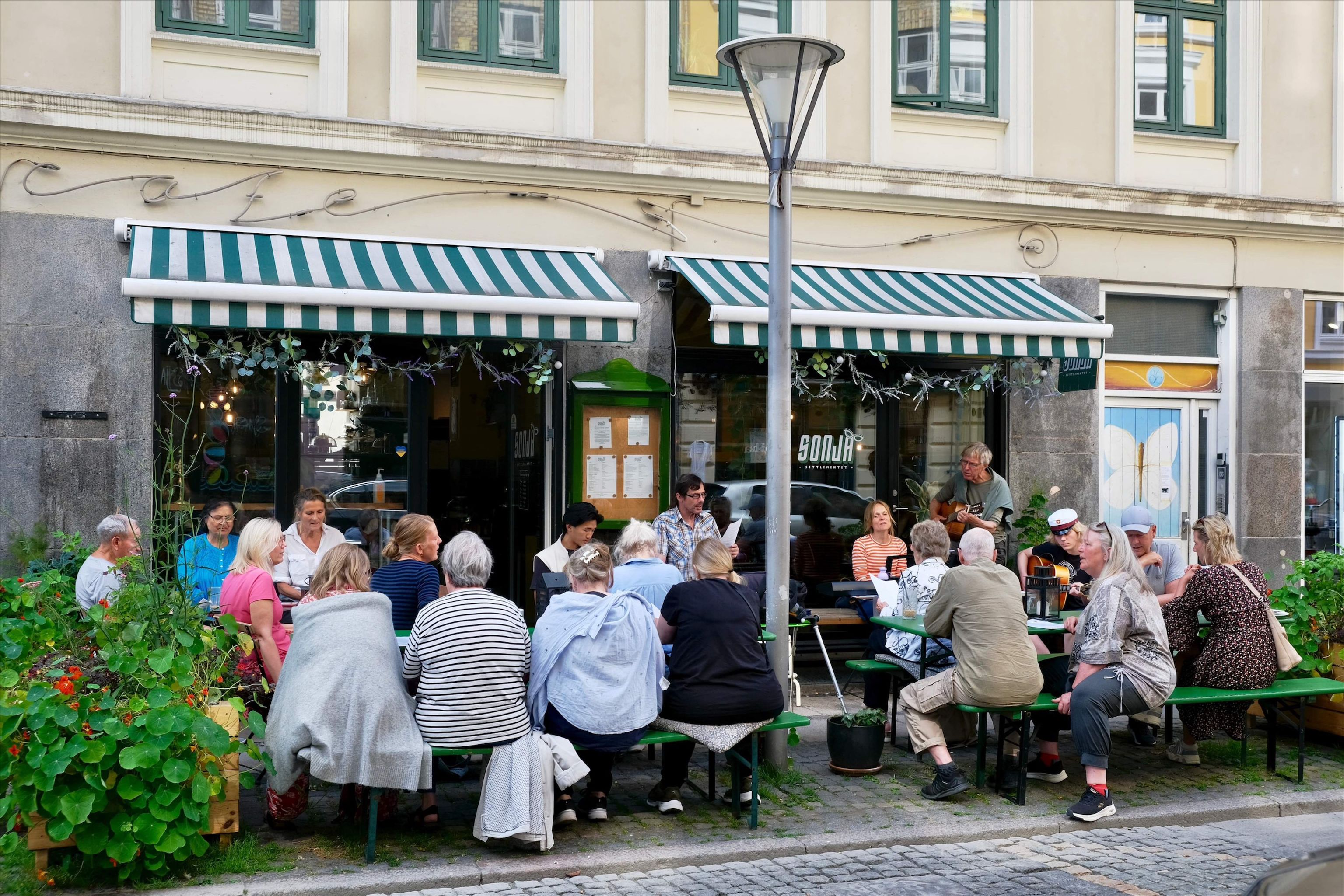 en gruppe mennesker sidder ved borde udenfor en restaurant.