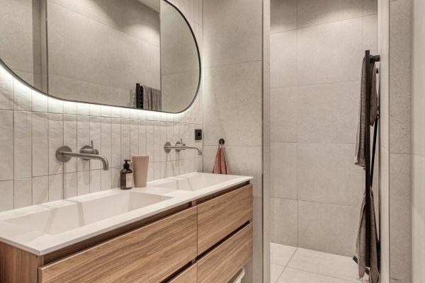 Badkamer in Voorburg met eiken dubbel wastafelmeubel, gebogen spiegel en inloopdouche