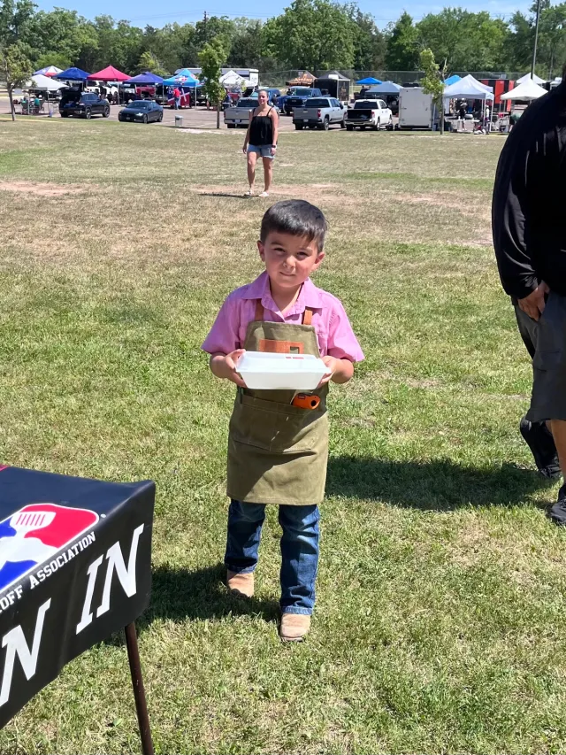 A young cook carries a turn-in container across the competition field.