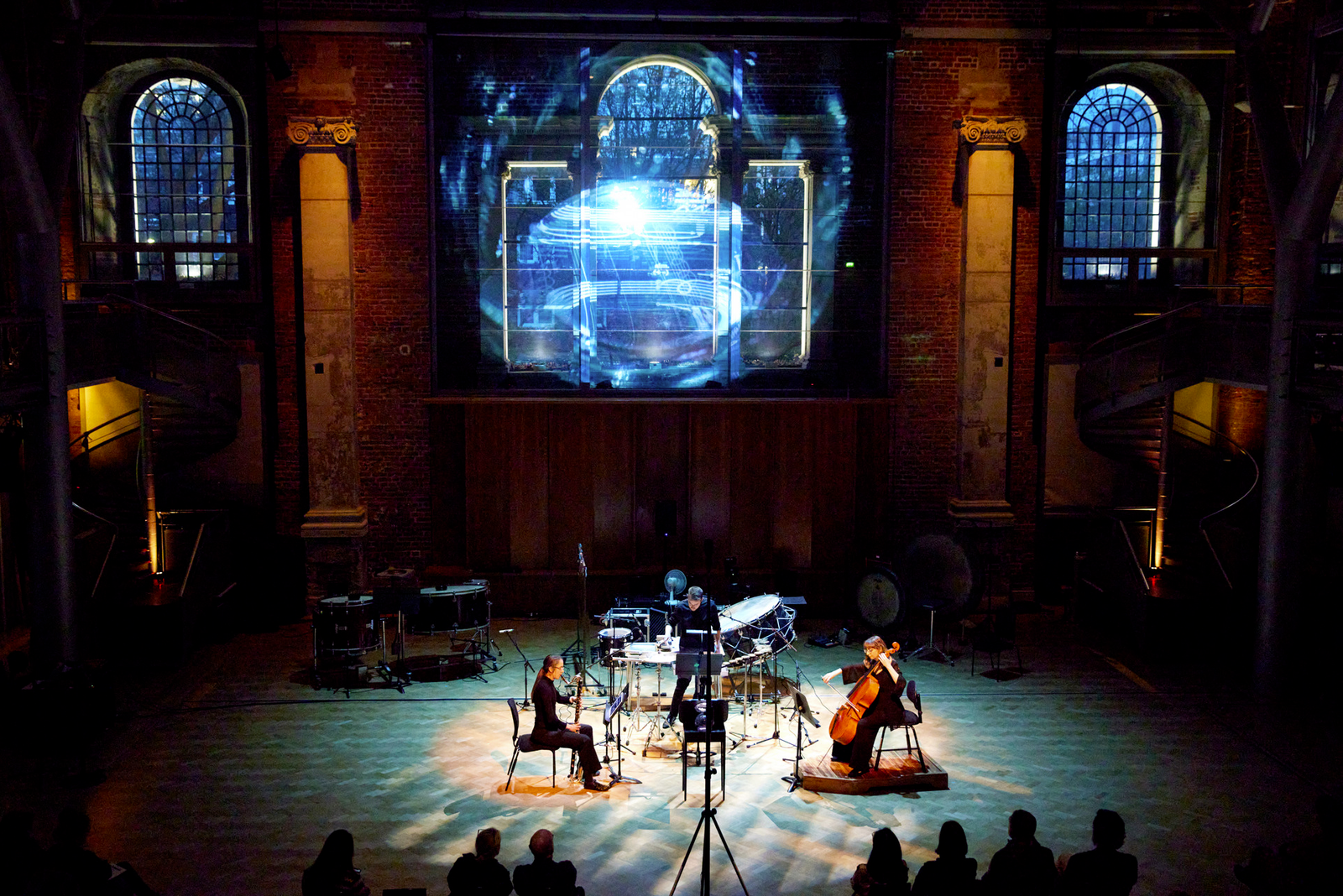 A chamber trio are arranged around a crystal-ball sculpture. A projection hovers above them, reflected off the arch windows. 