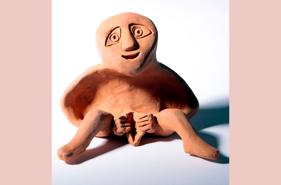 A terracotta Sheela-na-gig sits with her legs apart and her vulva splayed - she is a symbol of fertility 