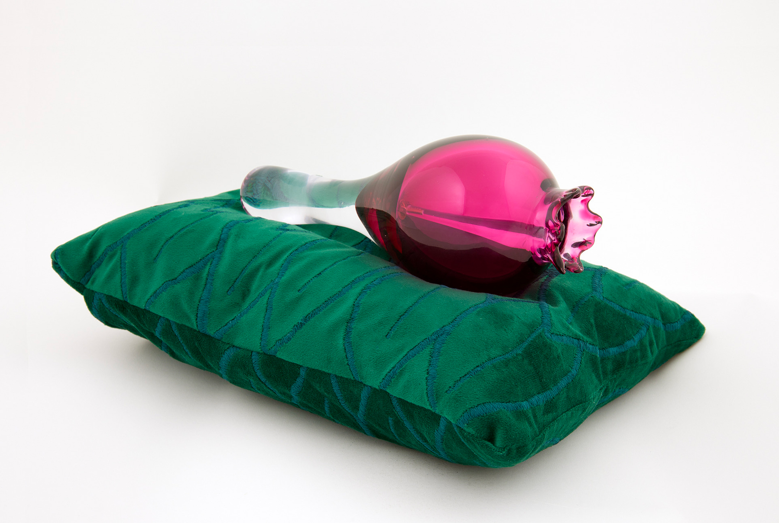 A glass pomegranate bell on a green velvet cushion, with leaf embroidery