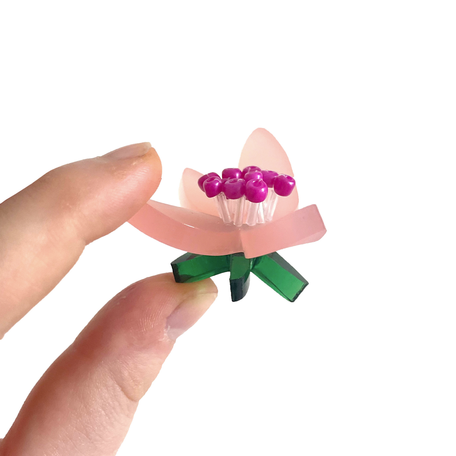 Flower plastic model held between two fingers on a white background. The petals are frosted pink with green leaves. 