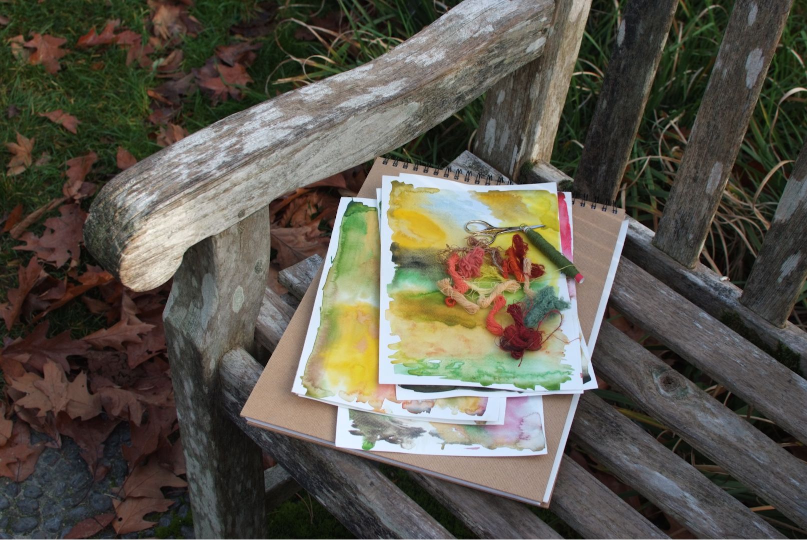 Photo of park bench with watercolour paintings on a notepad with woollen textile scraps on top