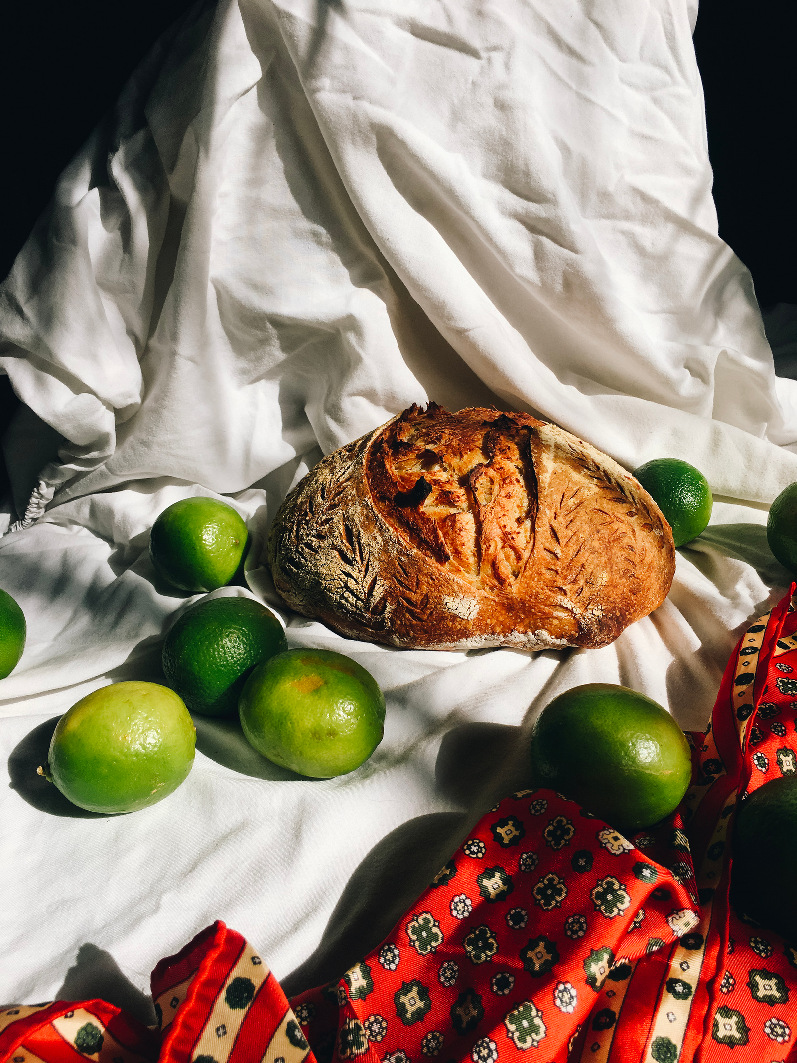 A loaf of bread and limes on white fabric