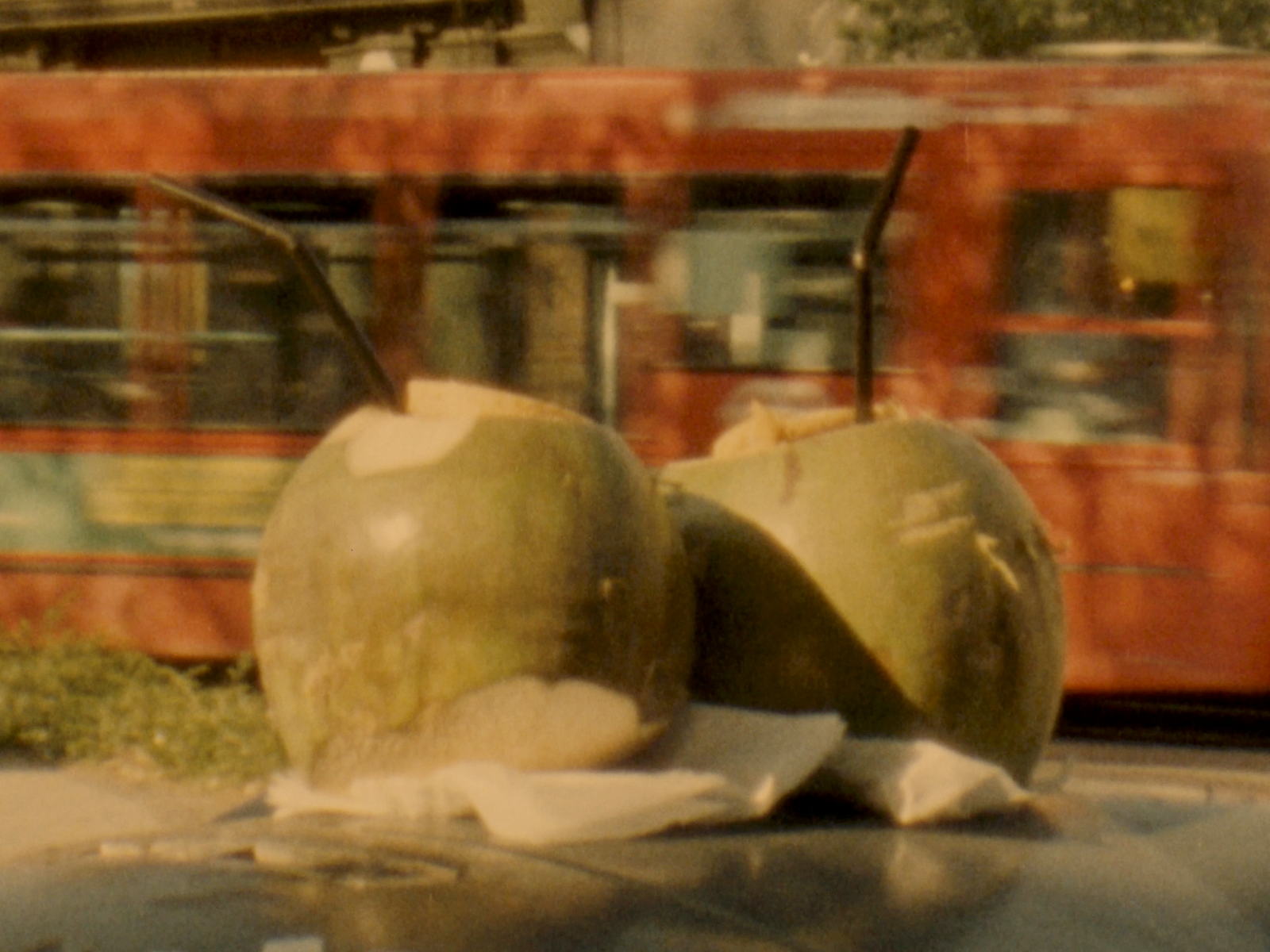 Still of two coconuts with straws on top of a bin with a bus going by in the background shot on super 8