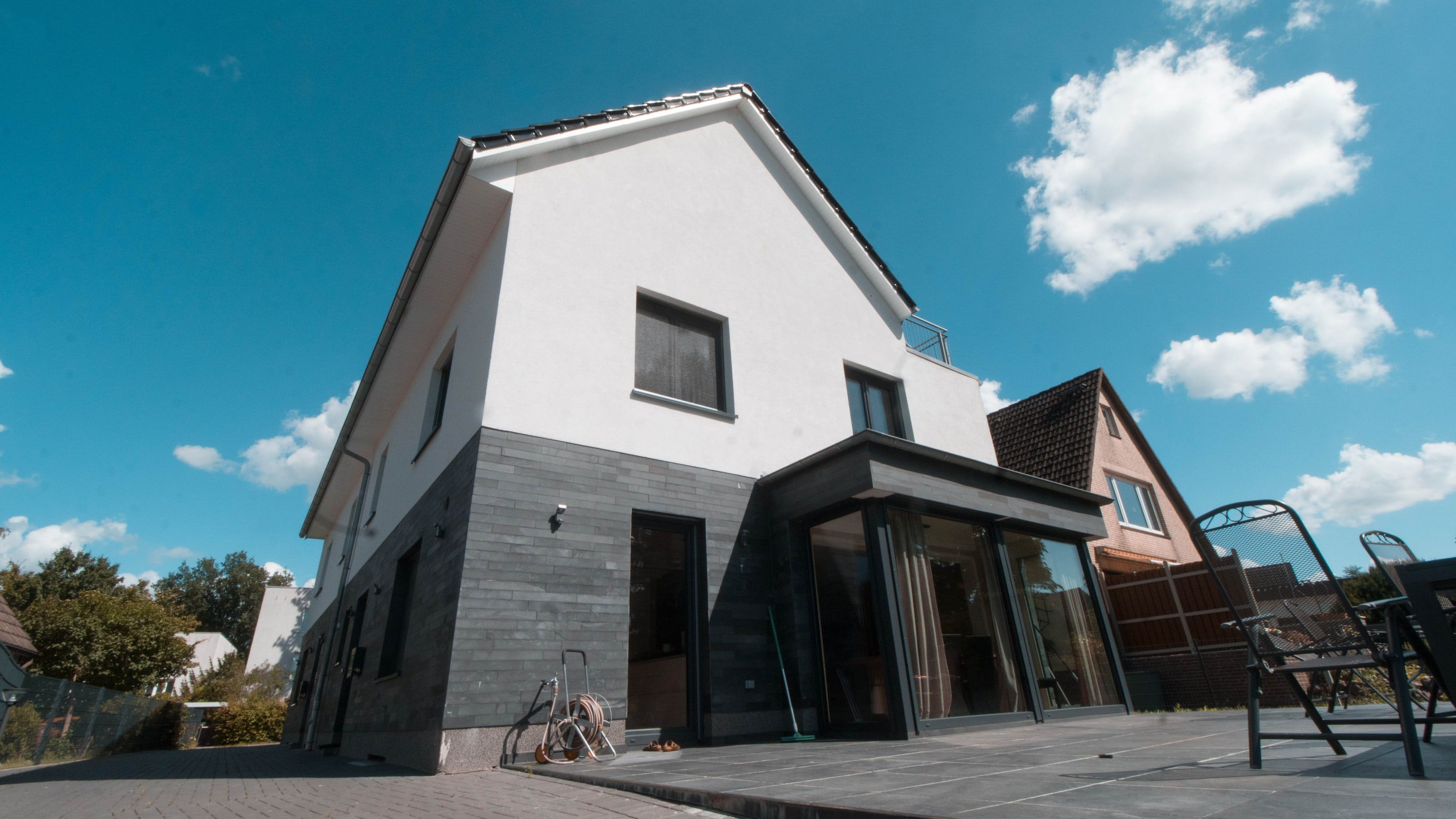 Doppelhaus mit weißem Obergeschoss und dunkel verkleidetem Erdgeschoss