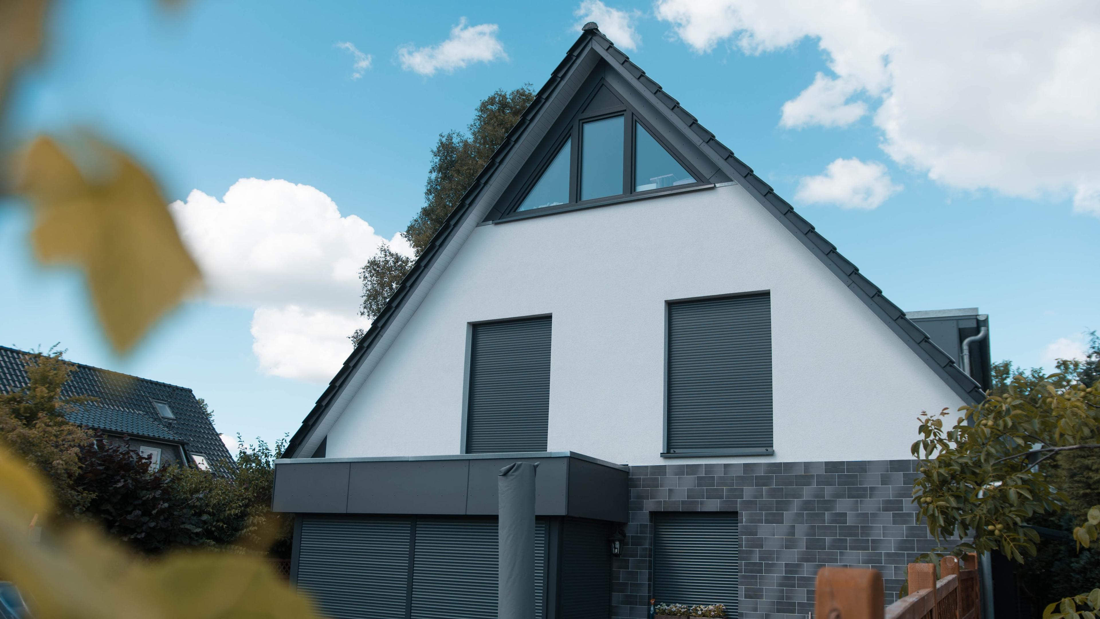 Doppelhaushälfte mit weißem Giebel, dunklem Sockel und Garage