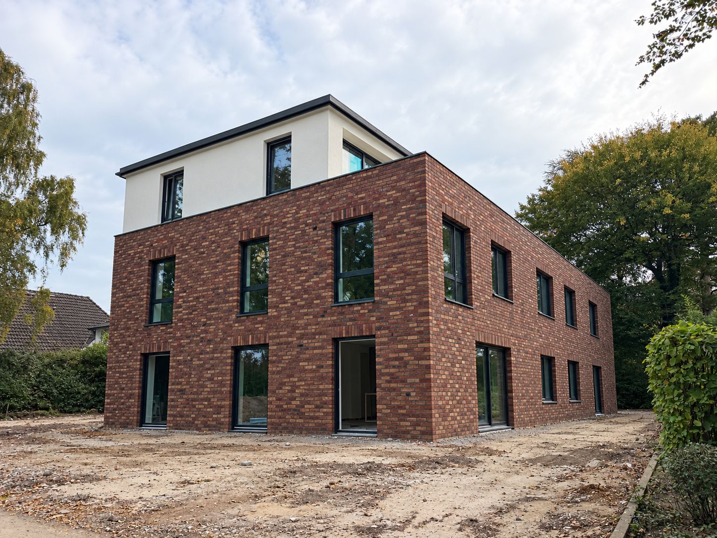 Rohbau eines Mehrfamilienhauses in Hamburg-Blankenese: Klinkerfassade, weiß verputztes Staffelgeschoss, eingebaute Fenster