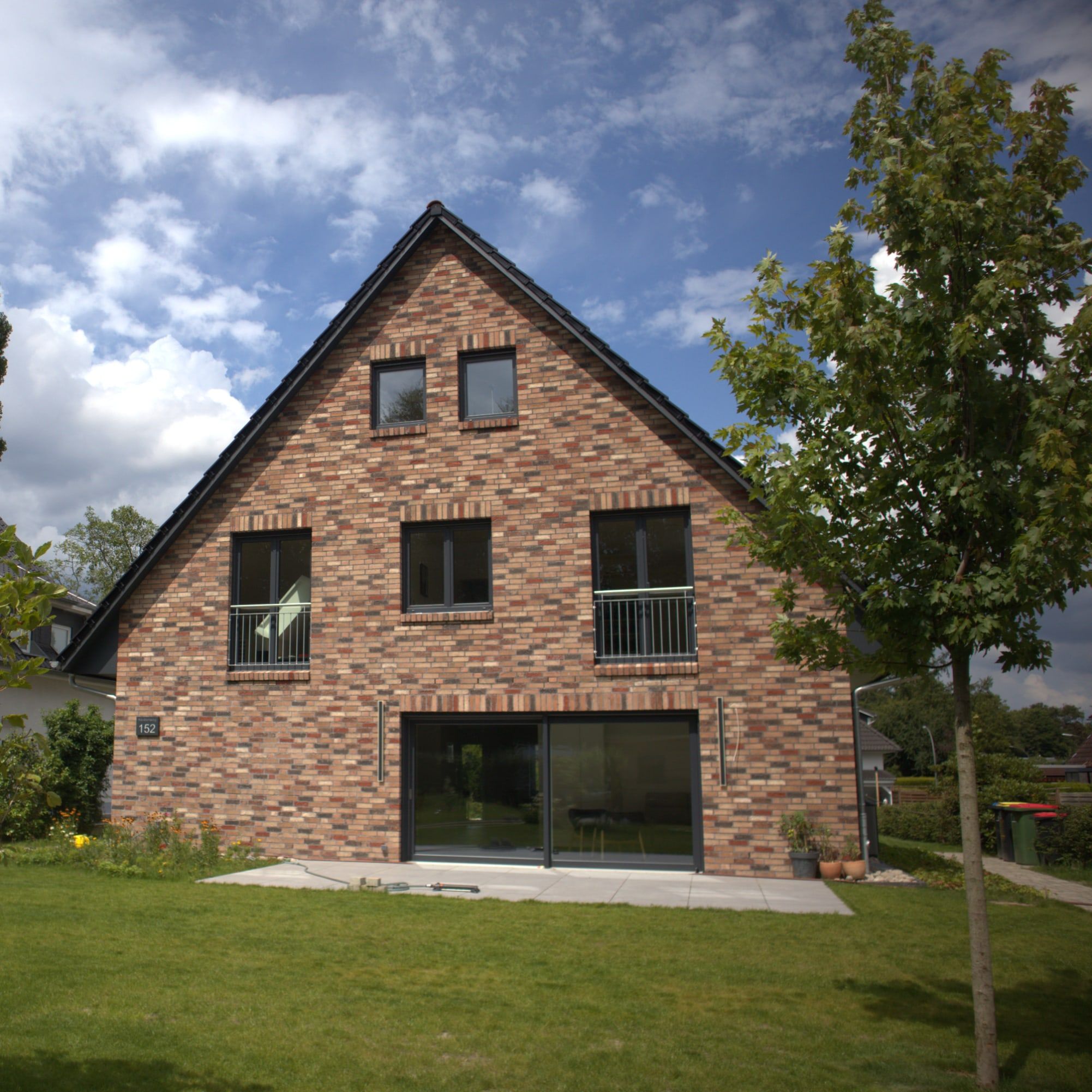 Einfamilienhaus mit rotem Klinker, Steildach und großen Fenstern zum Garten