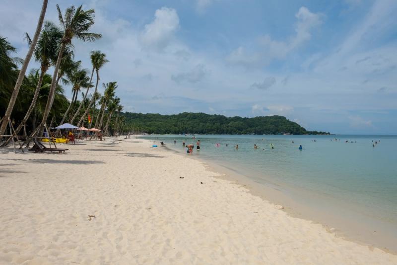 Palm-lined sandy shore and people in the water in the Khem Beach collection