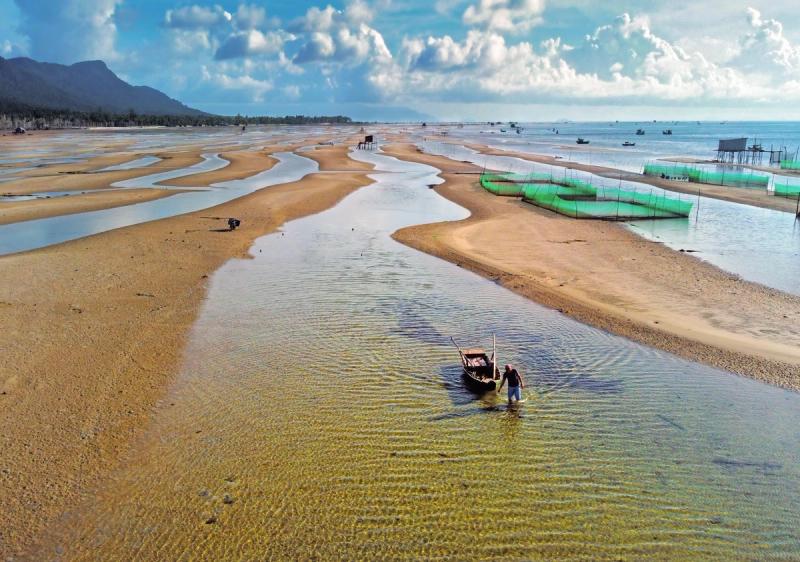 A person working in the shallow water beside sandbars
