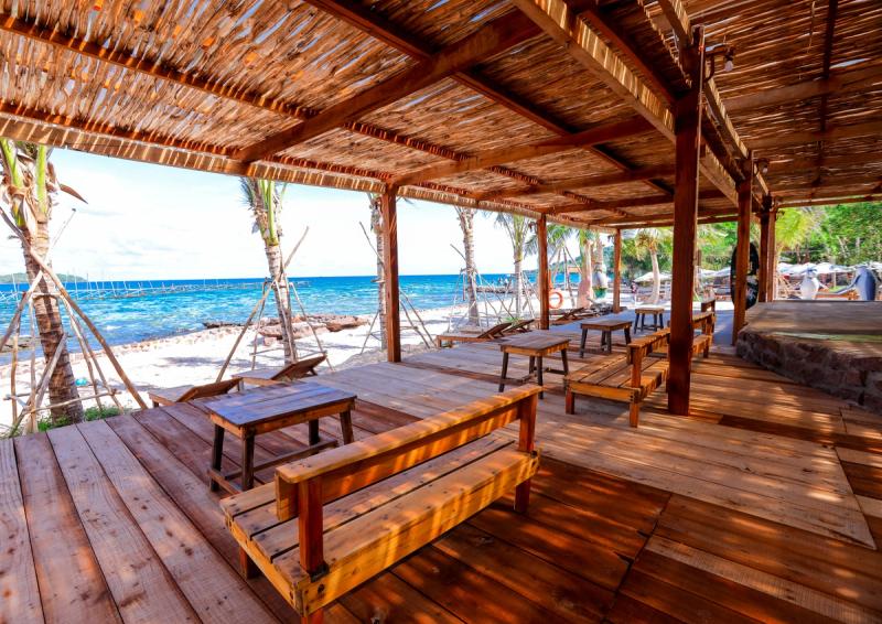 Bench tables under a thatched roof beside the sea at Dugong Beach Bar