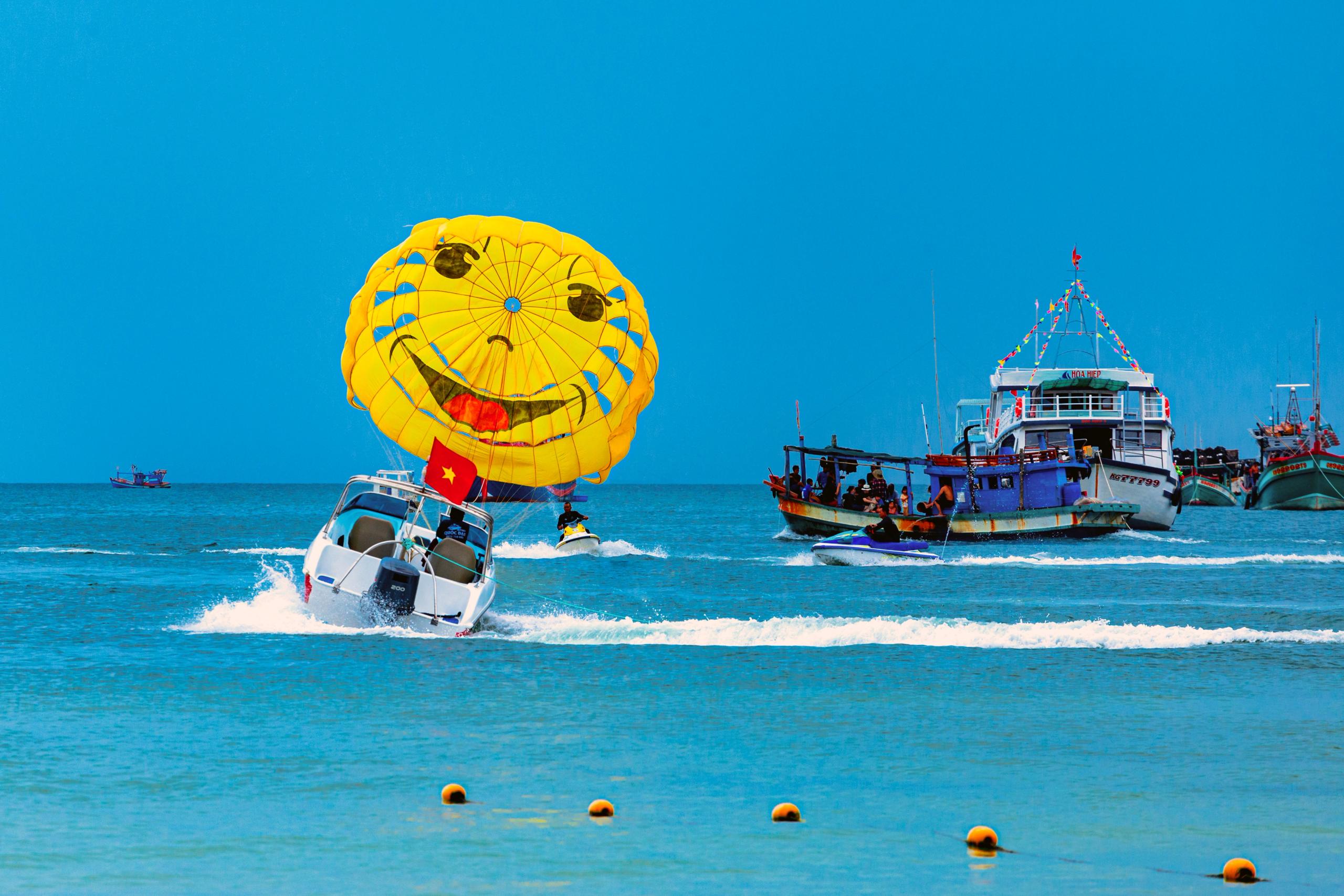 A yellow parasail above the sea with a motorboat and nearby boats