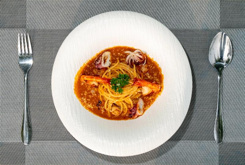 Pasta with prawns and squid pieces in reddish sauce on a white plate