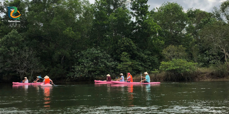 Kayakers beside the wooded banks of Cua Can River