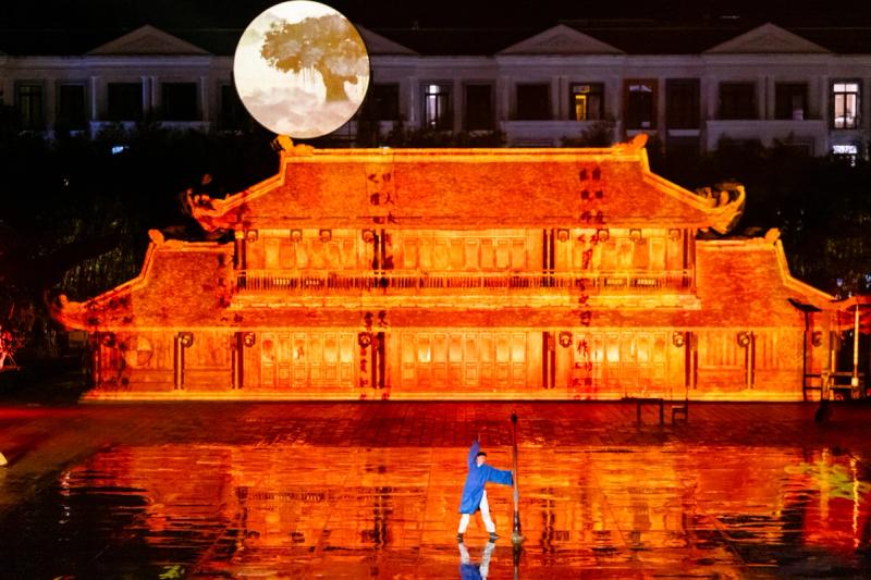 Moon projection and a blue-clad performer on the courtyard stage