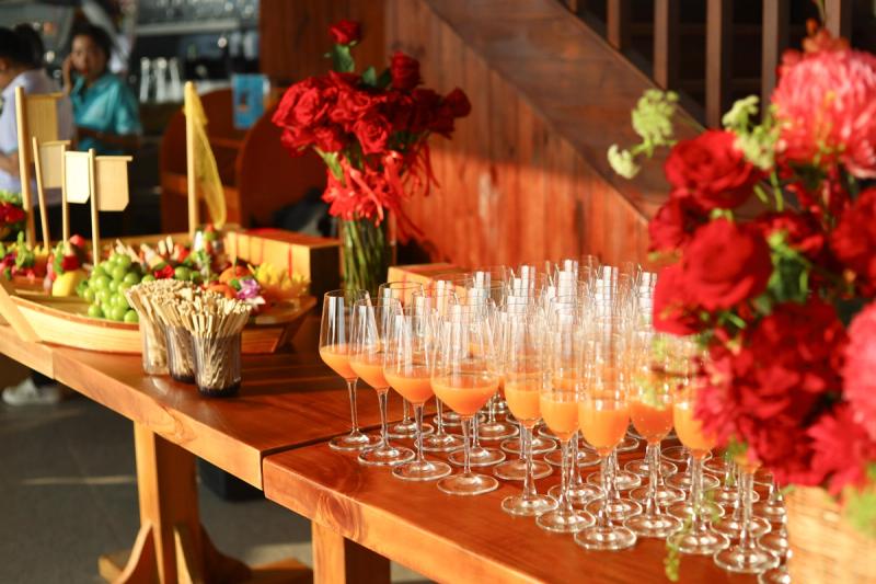 Rows of orange drinks with fruit and red flowers on a wooden table