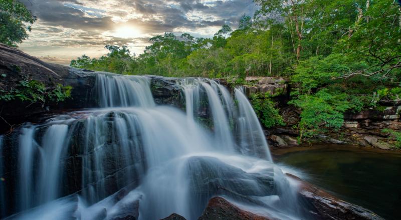 Water cascading over rocks amid forest beneath a bright sky