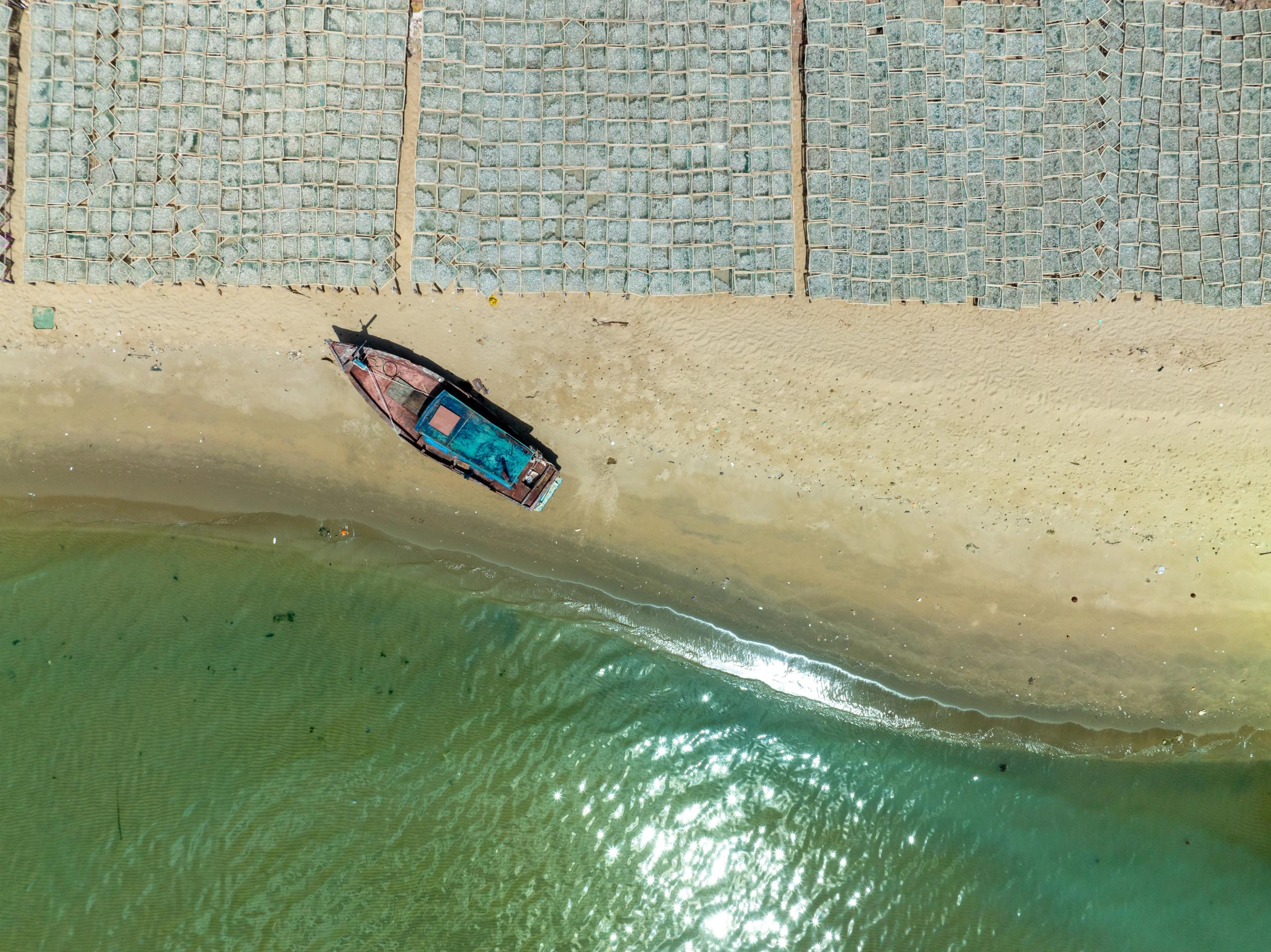 A fishing boat on sand below rows of drying racks