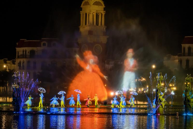 Costumed performers and fountains beneath a European-style clock tower in the Colors of Venice collection