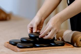 A therapist arranging massage stones on a wooden tray