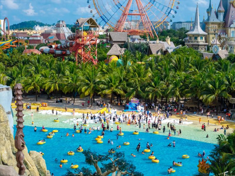Visitors with yellow inflatable rings in a large pool below themed buildings