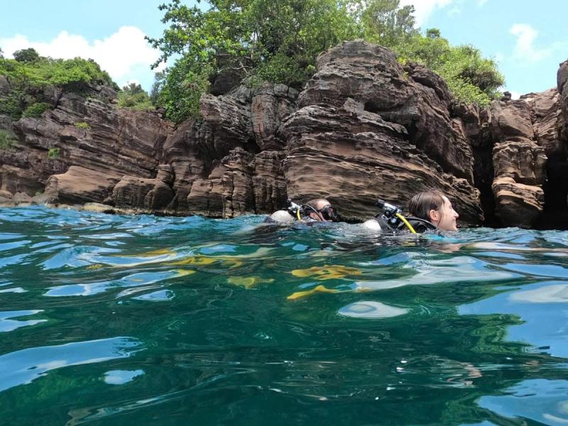Divers with tanks at the surface beside coastal rocks