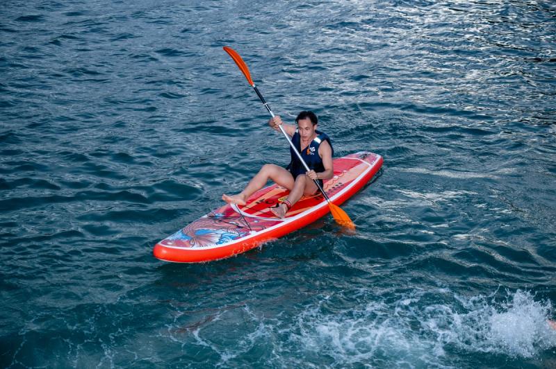 A seated paddler wearing a flotation vest on a red board