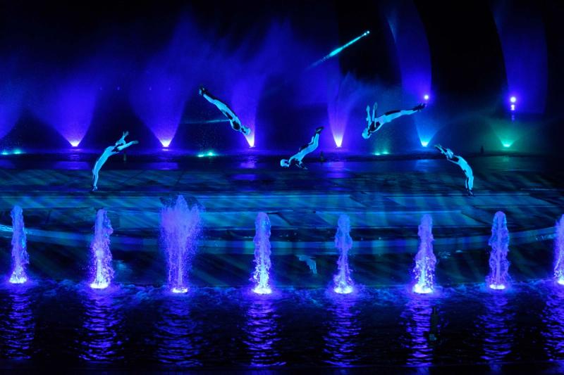 Acrobatic performers above blue-lit stage water